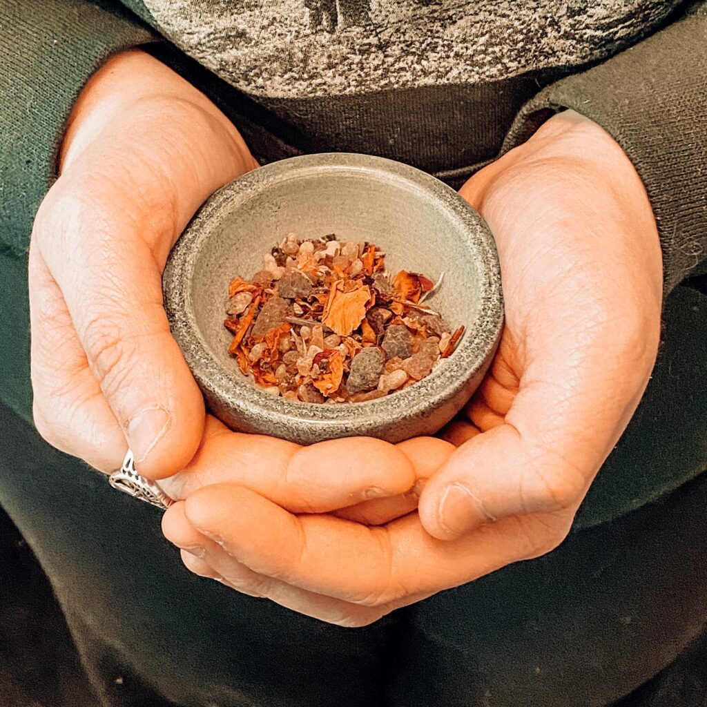 A close-up of a woman's hands, which cup a mortar bowl containing some hand-blended incense. Photograph Credit: Heather K Veitch